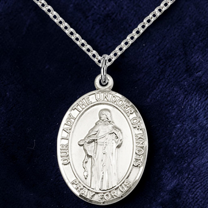 Silver religious pendant on a chain against a dark blue background
