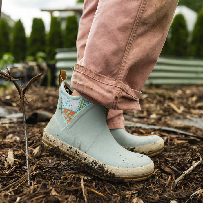 Light blue waterproof rain boots with floral pattern worn by a person in a garden setting.