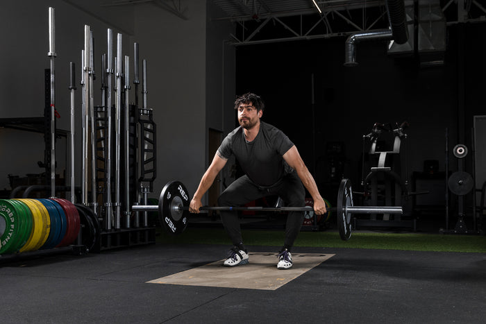 Athlete hang lifting a barbell with Black Competition Bumper Plates (KG)