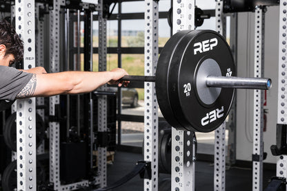 Athlete holding a barbell with Black Competition Bumper Plates (KG) on the front of a PR-5000 rack