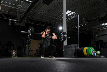 Athlete hang cleaning a barbell with Black Competition Bumper Plates (LB)