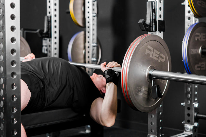 An athlete bench pressing in a PR-5000 rack with Rep Fitness Calibrated Steel Plates (LB) loaded on the barbell