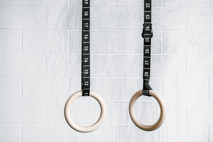 REP’s Competition Gymnastic Straps and Wood Rings hanging in front of a gym wall