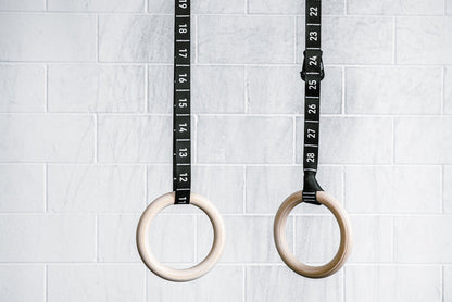 REP’s Competition Gymnastic Straps and Wood Rings hanging in front of a gym wall