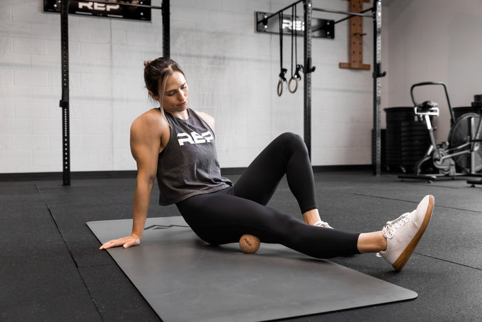 Action-shot: Athlete targeting a pressure point on their leg by rolling the REP Cork Massage Ball against the floor.