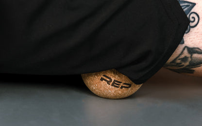 Close-up: Athlete targeting a pressure point on their leg by rolling the REP Cork Massage Ball against the floor.