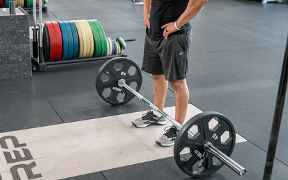 Male lifter standing above a loaded REP Delta Basic Bar on an Olympic lifting platform.
