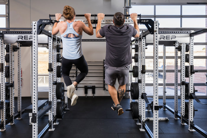 Two athletes doing a pull-up from the REP Fitness Double Pull-Up Bar on an 82 inch crossmember