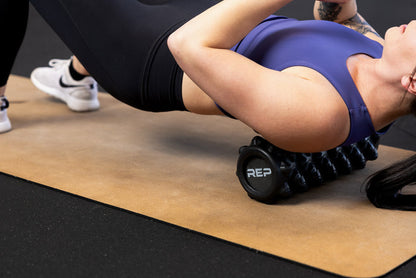 Person using High Density Foam Roller to roll out their upper back on a cork yoga mat.