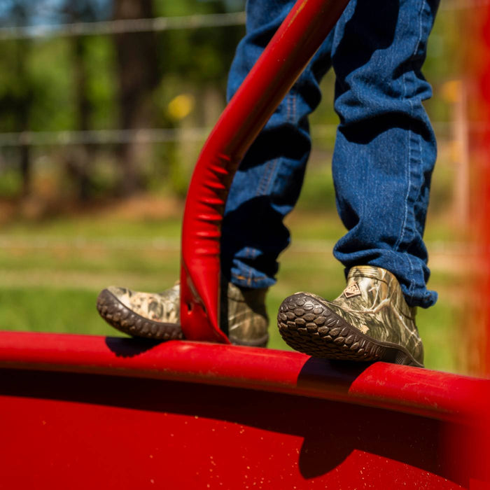 Mini Muck Kids Rain Boot in Mossy Oak Country DNA MLBCMDNA standing on a red playground swing