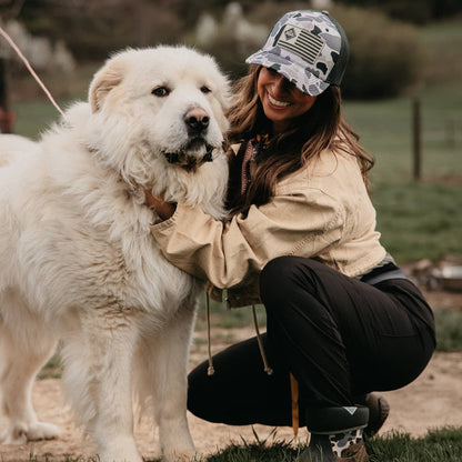 Woman with a large great pyrenees dog in a farm setting wearing a duck camo muck boots logo hat.