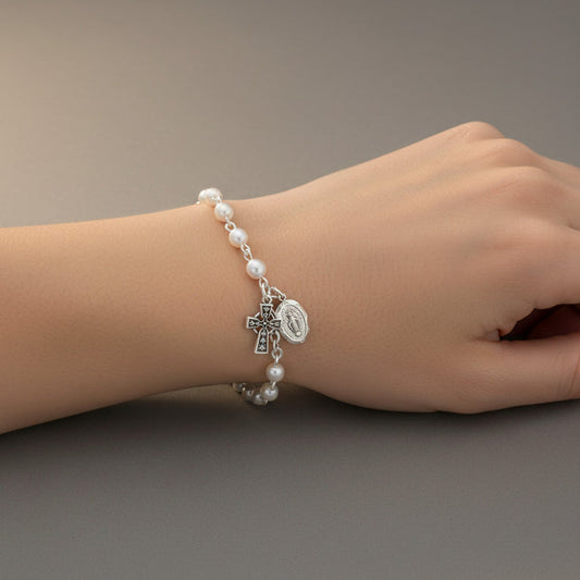 Pearl bracelet with charms on a wrist against a neutral background