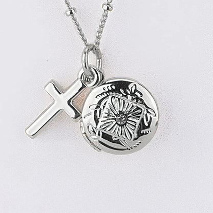 Silver necklace with a cross pendant and round locket on a light gray background