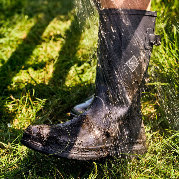 Black rubber boot splashing in water on a grassy background