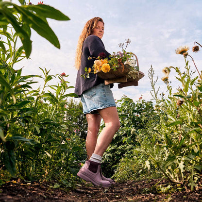 Woman holding a basket of flowers in a garden wearing pink rubber boots