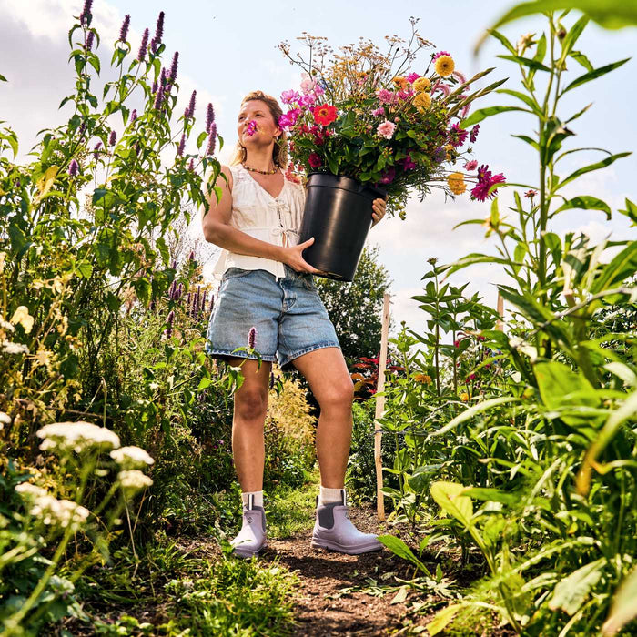Woman holding a large bucket of flowers in a garden wearing Muck Boots Rainscape Women's Chelsea Rain Boots.