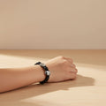 Hand wearing a black bracelet on a wooden surface with a beige background