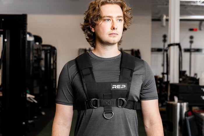 Person wearing a black REP fitness Sled Harness in a gym setting
