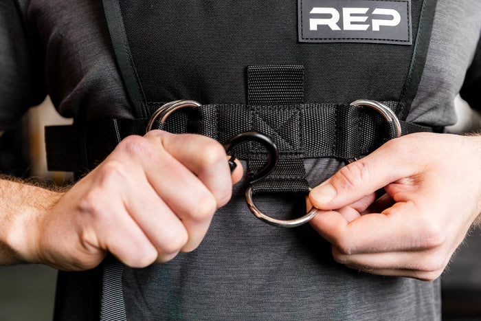 Person adding the Pull Strap to the front of the Sled Harness with 'REP' branding on a blurred background