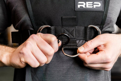 Person adding the Pull Strap to the front of the Sled Harness with 'REP' branding on a blurred background