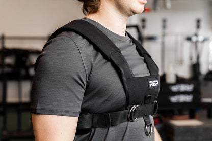 Person wearing a black Sled Harness with 'REP' branding in a gym setting
