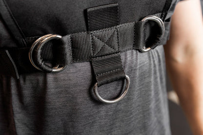 Close-up of a black Sled Harness with D-rings on a person wearing a gray shirt.