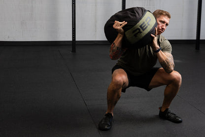 Person performing a squat with a weighted stone sandbag in a gym setting