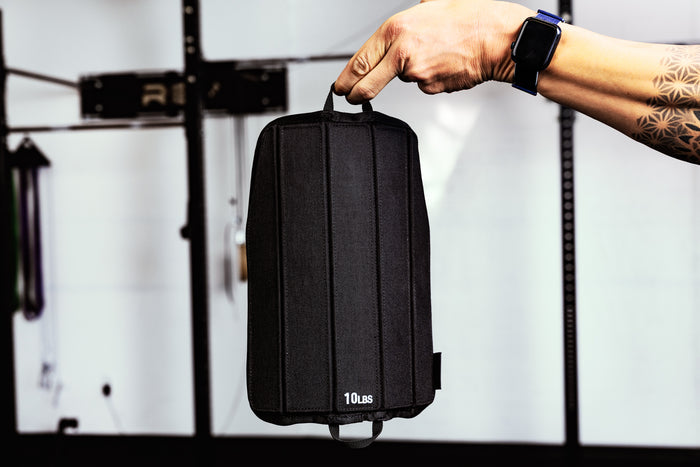 Person holding a black soft weight vest plate by loop  with '10Lus' branding against a blurred background