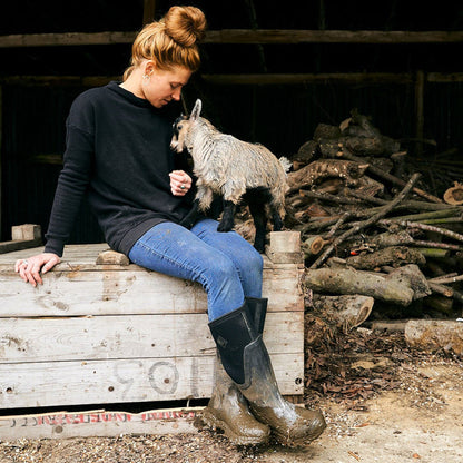 Woman sitting on a wooden crate with a small goat in a rustic setting