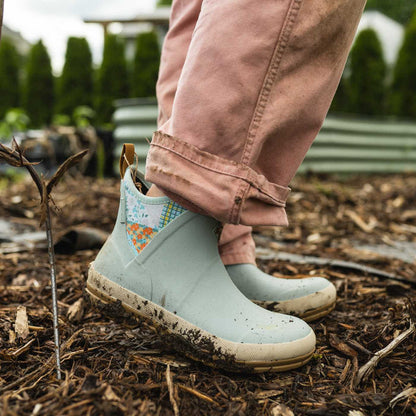 Light blue waterproof rain boots with floral pattern worn by a person in a garden setting.