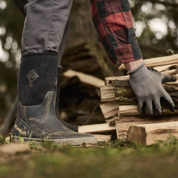MXP12M00  Person wearing Xplorer Men's Short Waterproof  Rubber Outdoor and a plaid shirt, stacking firewood outdoors.