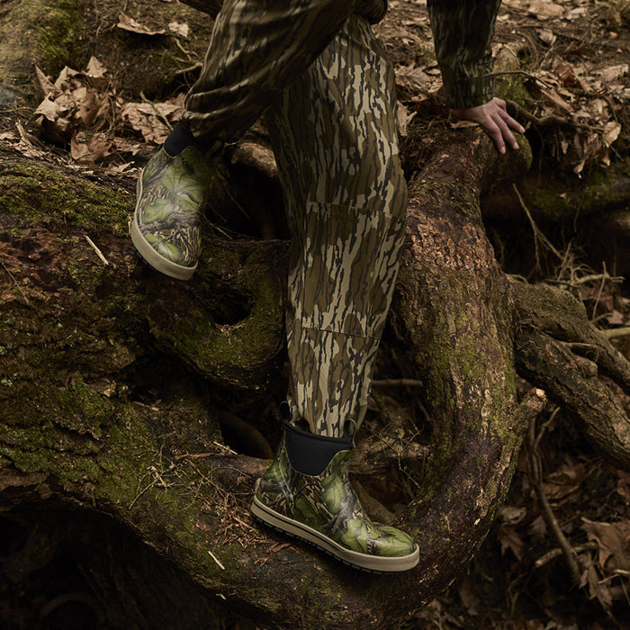 Person in camouflage gear climbing a fallen tree trunk in a forest setting