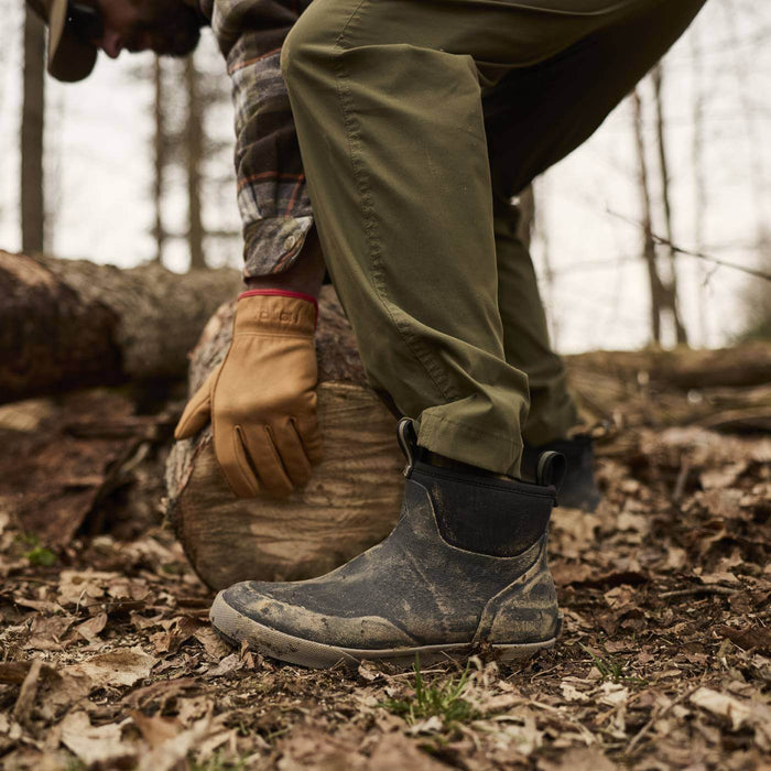 Person wearing green pants, brown gloves, and Men's Xplorer 6" Outdoor Ankle Boots in a forest setting.