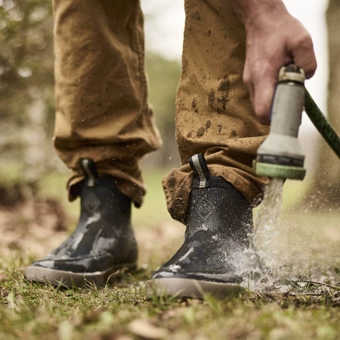 Person cleaning Xplorer 6" Men's Outdoor Ankle Boots with a hose outdoors